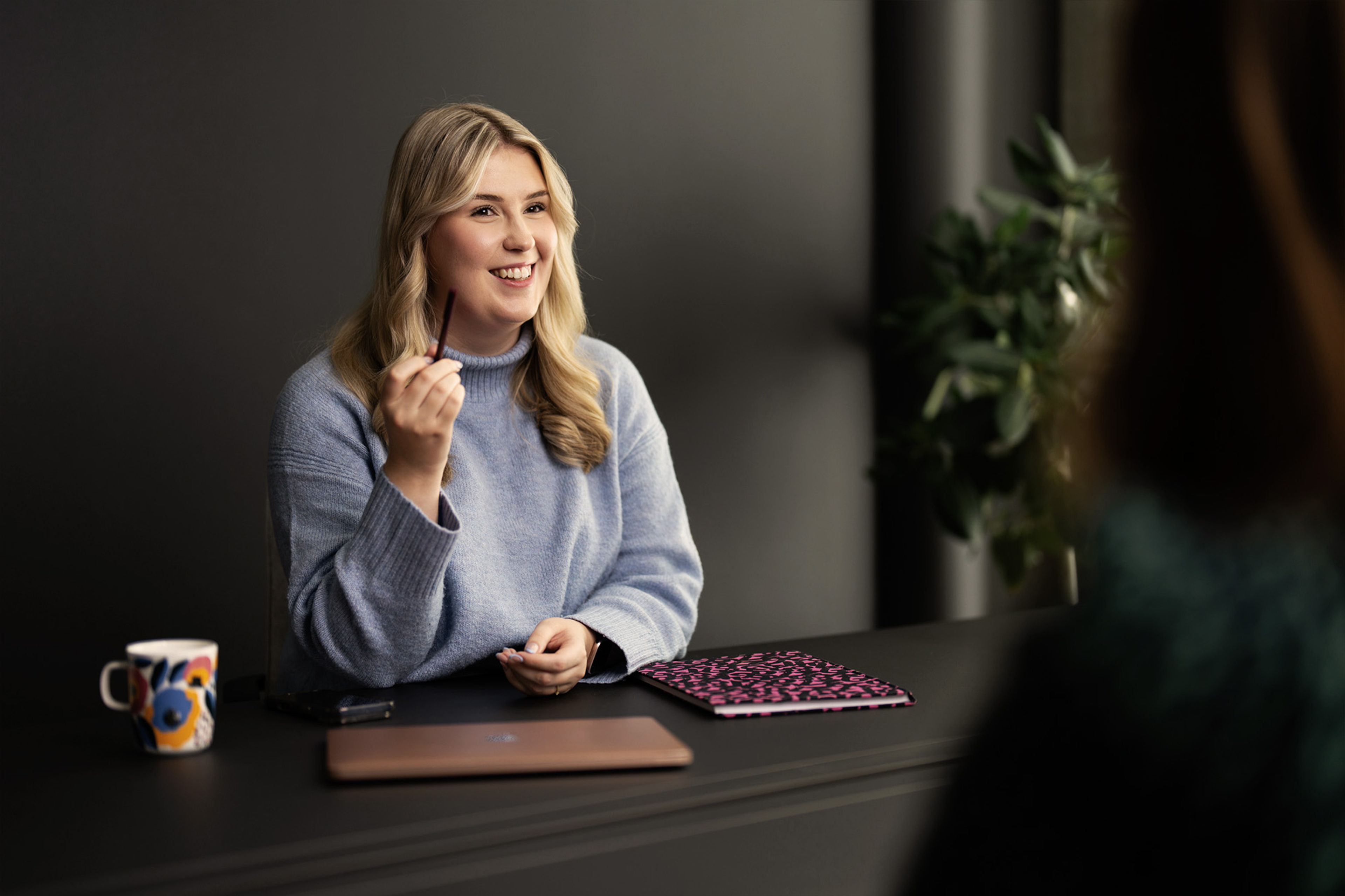 kvinna sitter vid ett skrivbord och pratar med en person.
