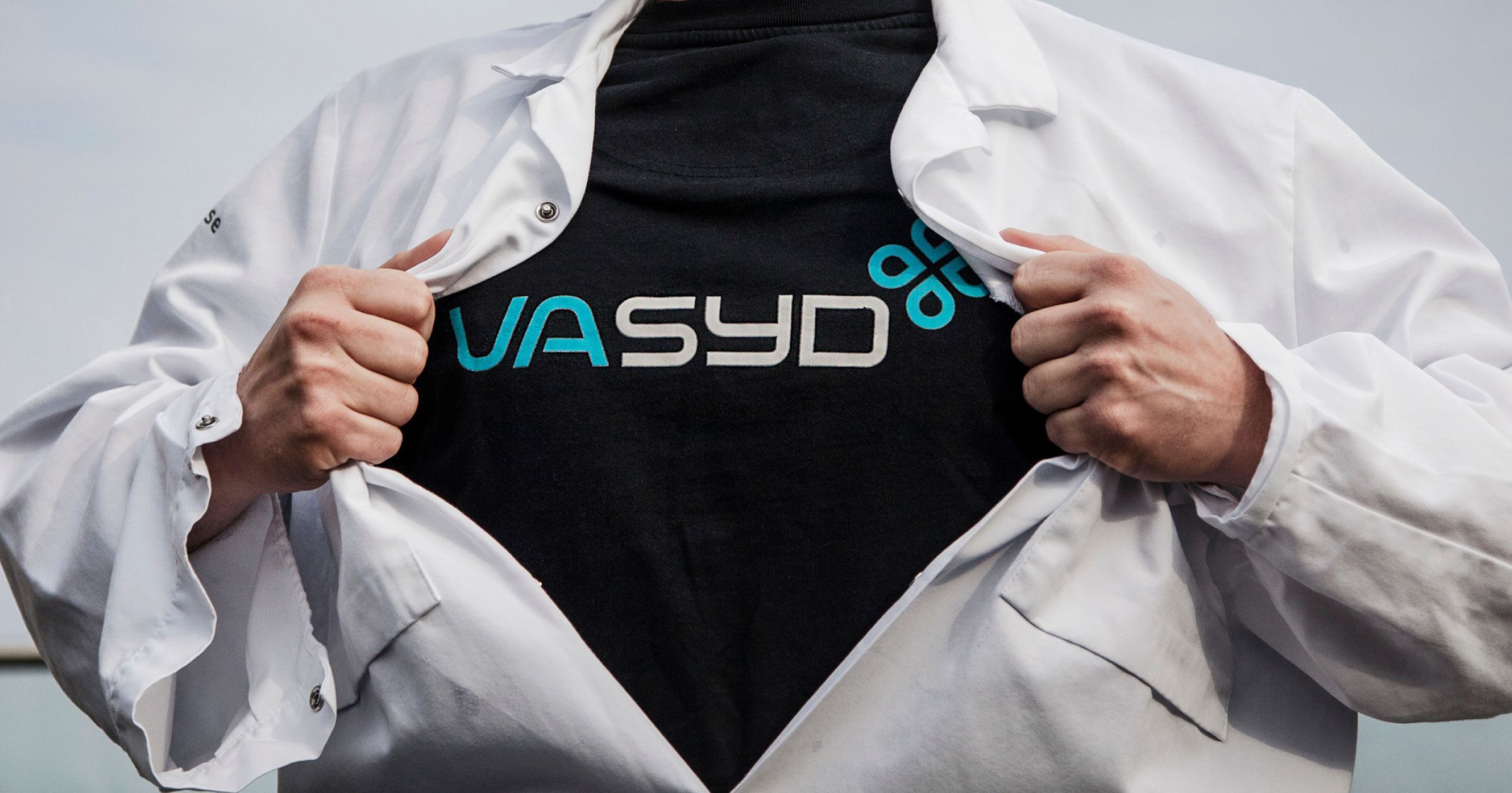Person i vit labbrock visar upp en svart tröja med VA SYD-logotypen.