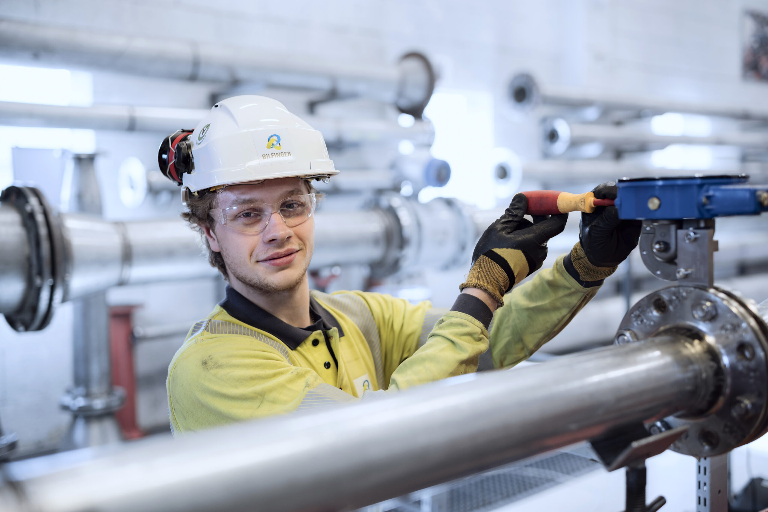 Industrimedarbetare i skyddsutrustning arbetar med rör och ventiler i en industrimiljö.