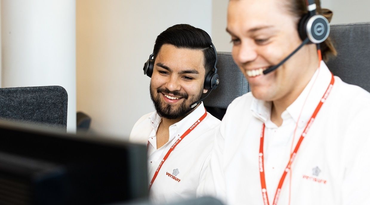 Två kollegor med headset arbetar tillsammans vid en dator på en arbetsplats.